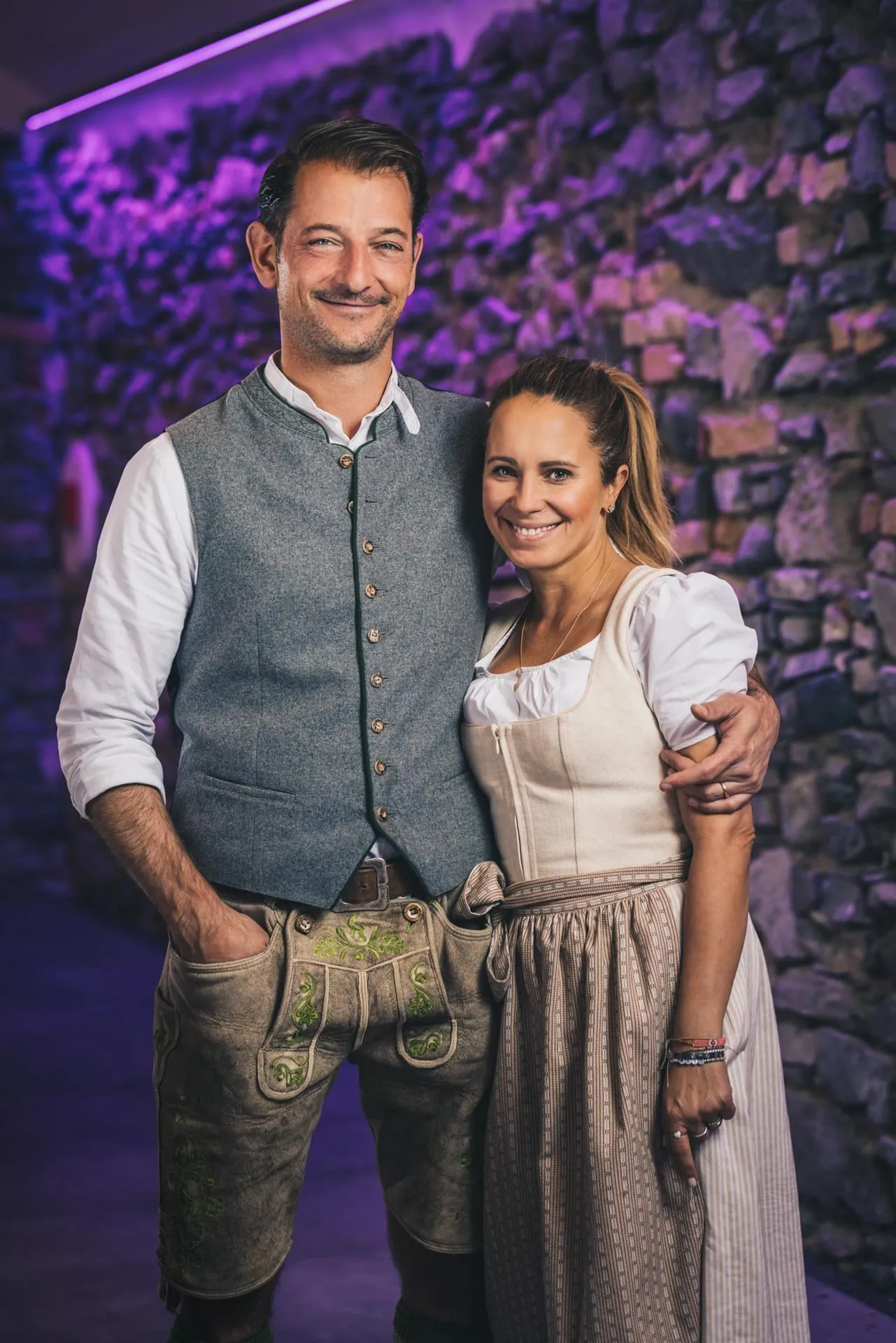 Gastgeberpaar in Tracht vor beleuchteter Steinwand, Hotel Klosterbräu